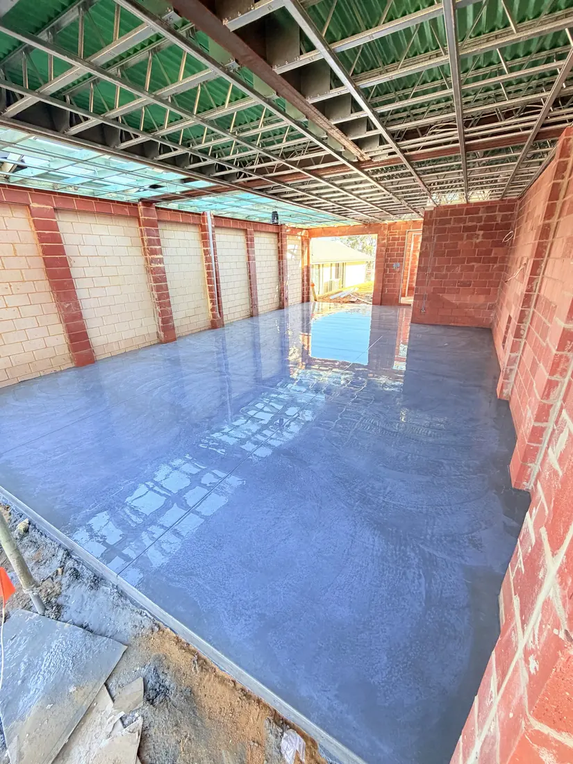 Fresh garage slab curing inside a new brick garage shell in Perth