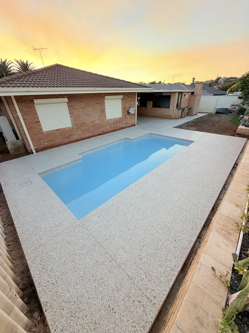White exposed aggregate pool surround around a backyard pool at sunset, Perth