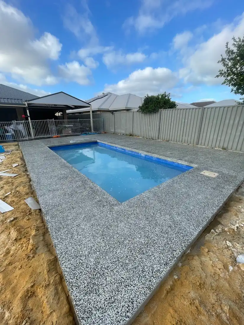 In-progress dark grey exposed aggregate surround around a compact Perth pool