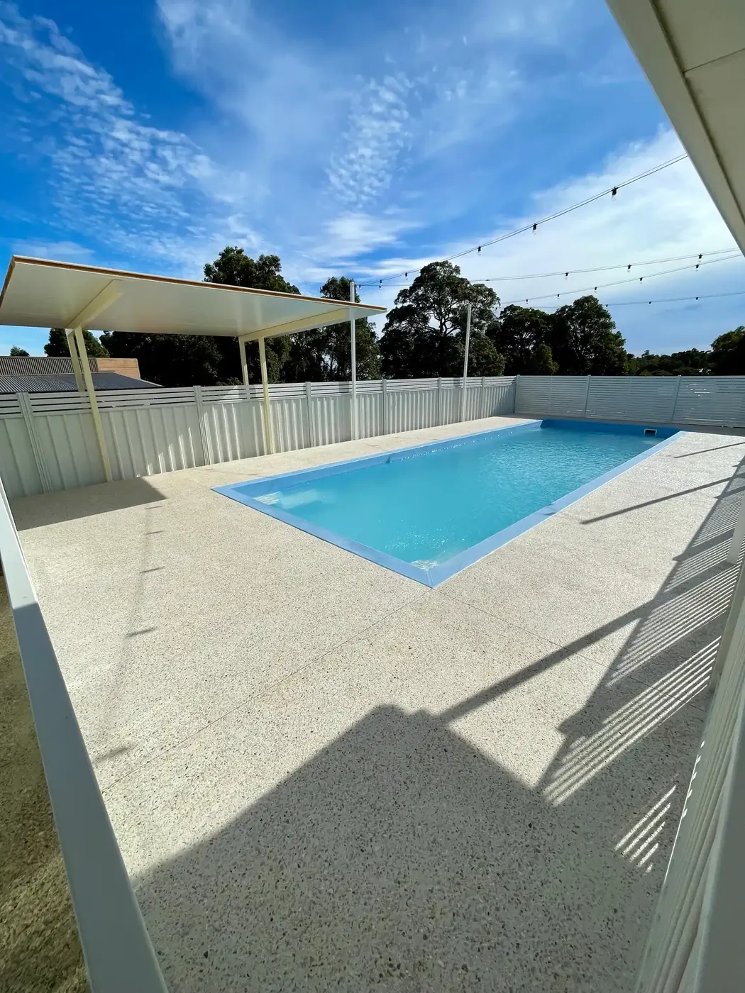 White exposed aggregate pool surround around a backyard pool, Perth