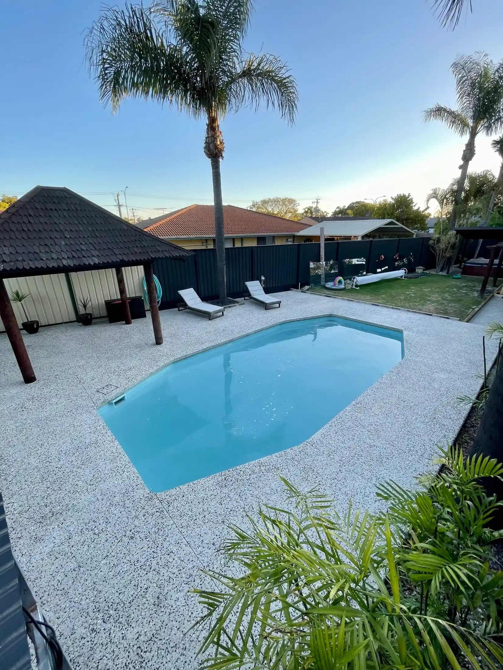 Exposed aggregate pool surround with sun loungers and palms, Perth