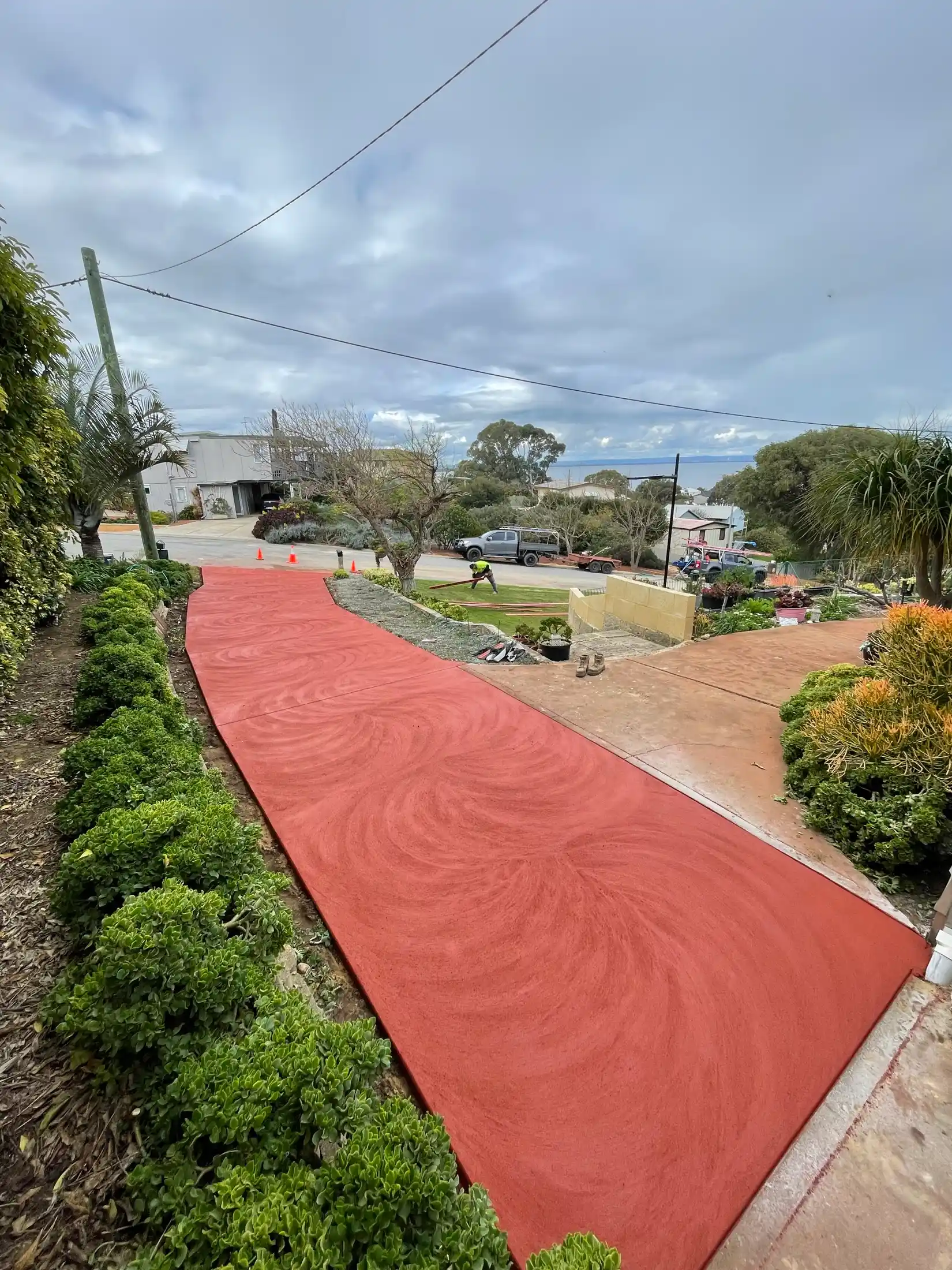 Long red coloured concrete driveway sweeping to a Perth home