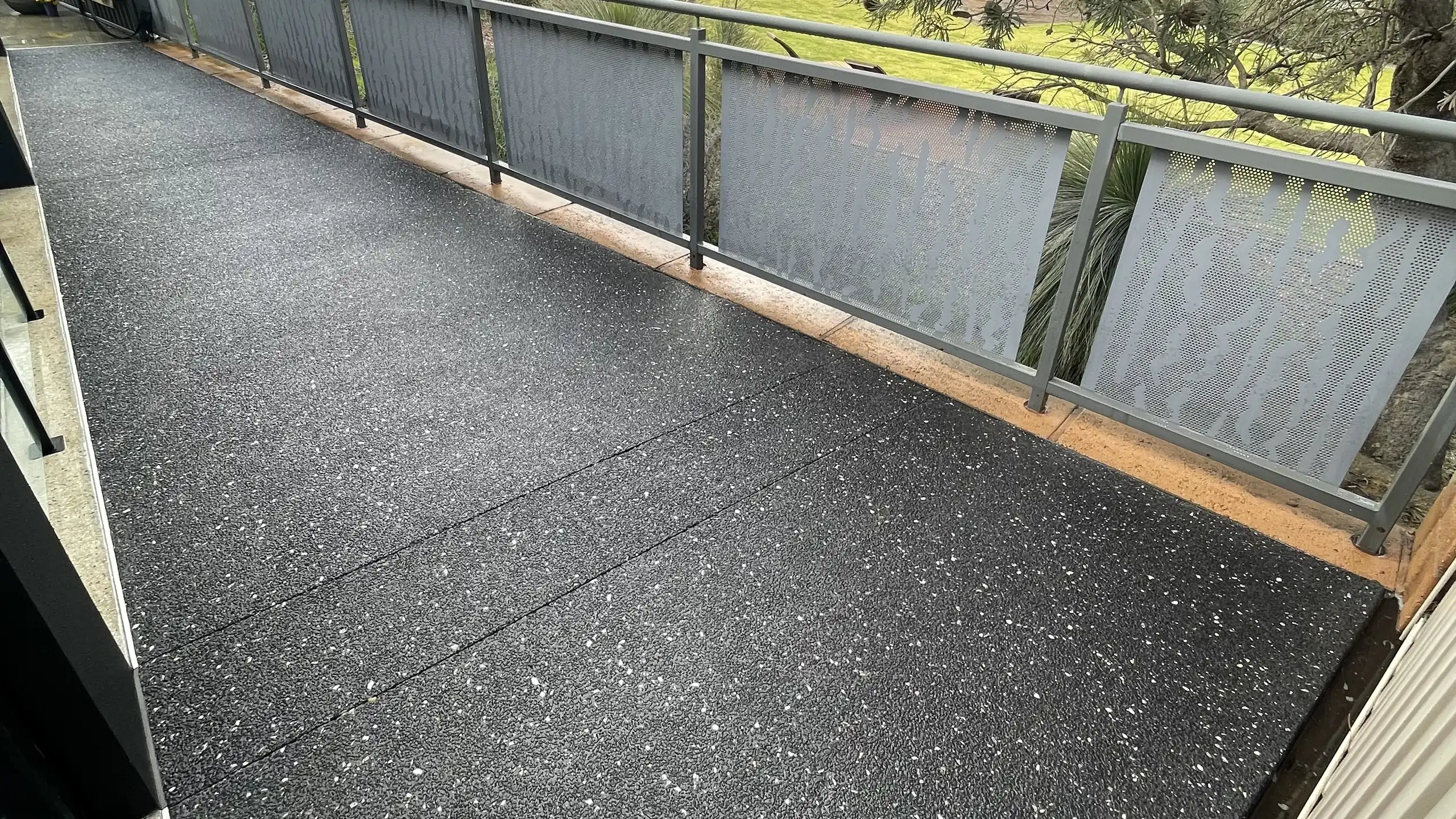 Charcoal exposed aggregate alfresco area beside a glass pool fence, Perth