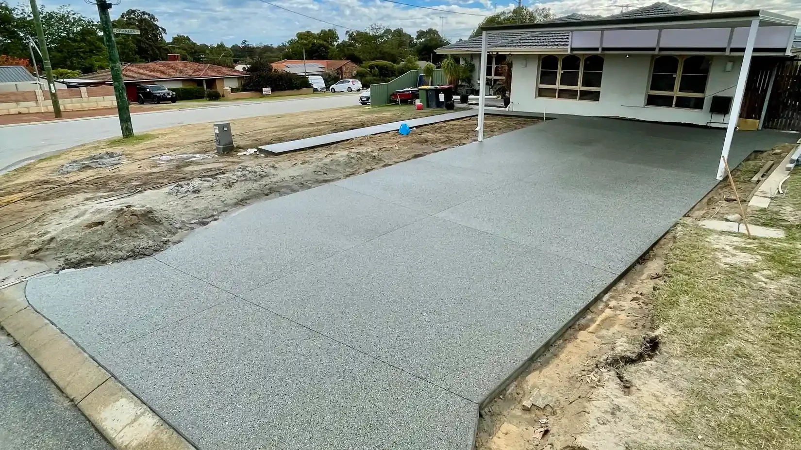 Finished grey exposed aggregate driveway beneath a Perth carport