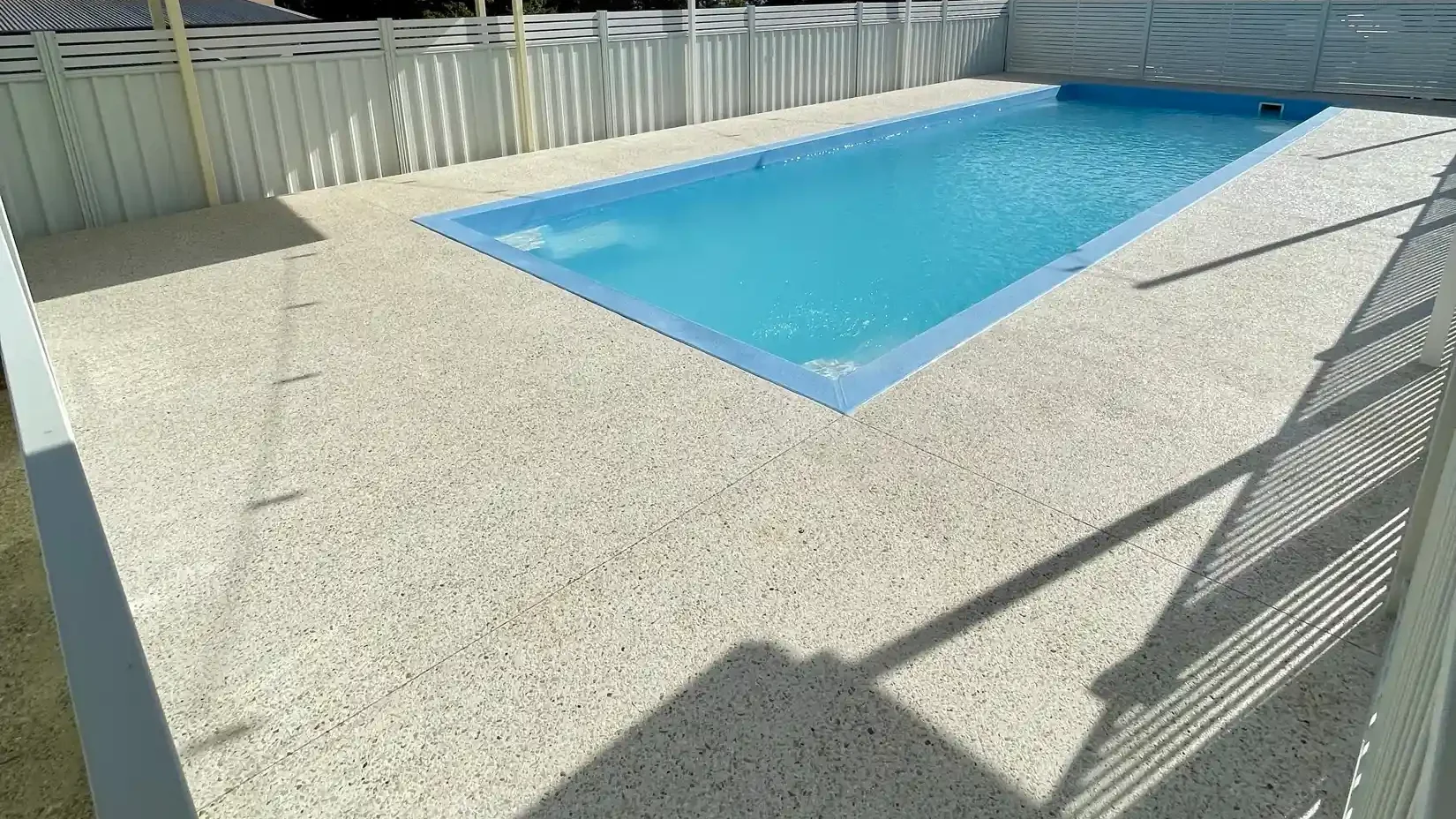Light exposed aggregate pool surround with white fencing and a shade canopy